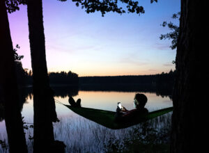 man in hammock near lake with phone in hands late evening