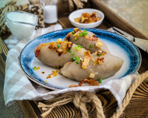 Traditional Lithuanian dish Zeppelin, boiled potato dumplings stuffed with minced pork, on a colored ceramic plate on a gray concrete background