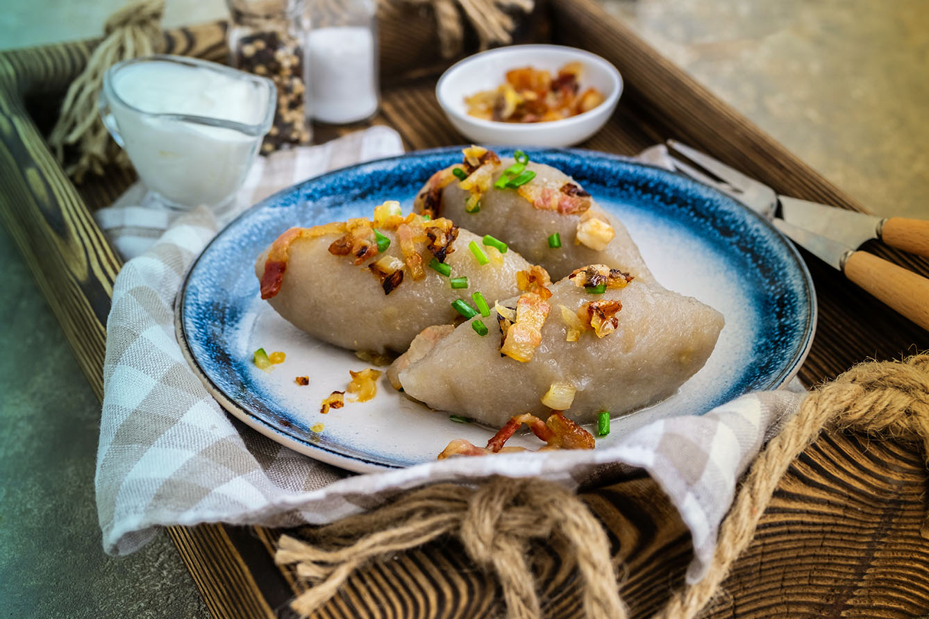Traditional Lithuanian dish Zeppelin, boiled potato dumplings stuffed with minced pork, on a colored ceramic plate on a gray concrete background