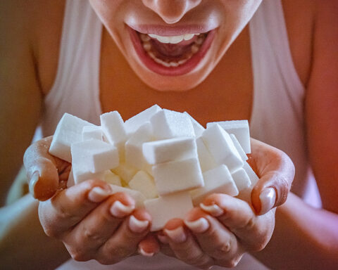 Close-up of woman holding a hands full of sugar cubes in front of her open mouth