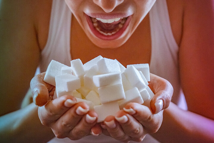 Close-up of woman holding a hands full of sugar cubes in front of her open mouth