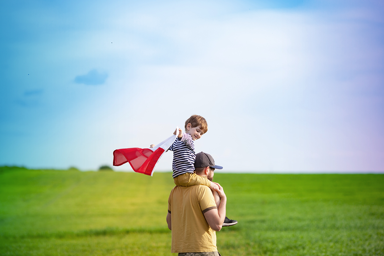 Dad with his little son walking in the field holding flag of Poland