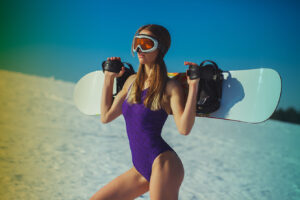Sexy woman in swim suit with snowboard on spring mountains