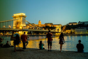 Tourists sit along the Danube river near the Chain bridge enjoying the view at sunset