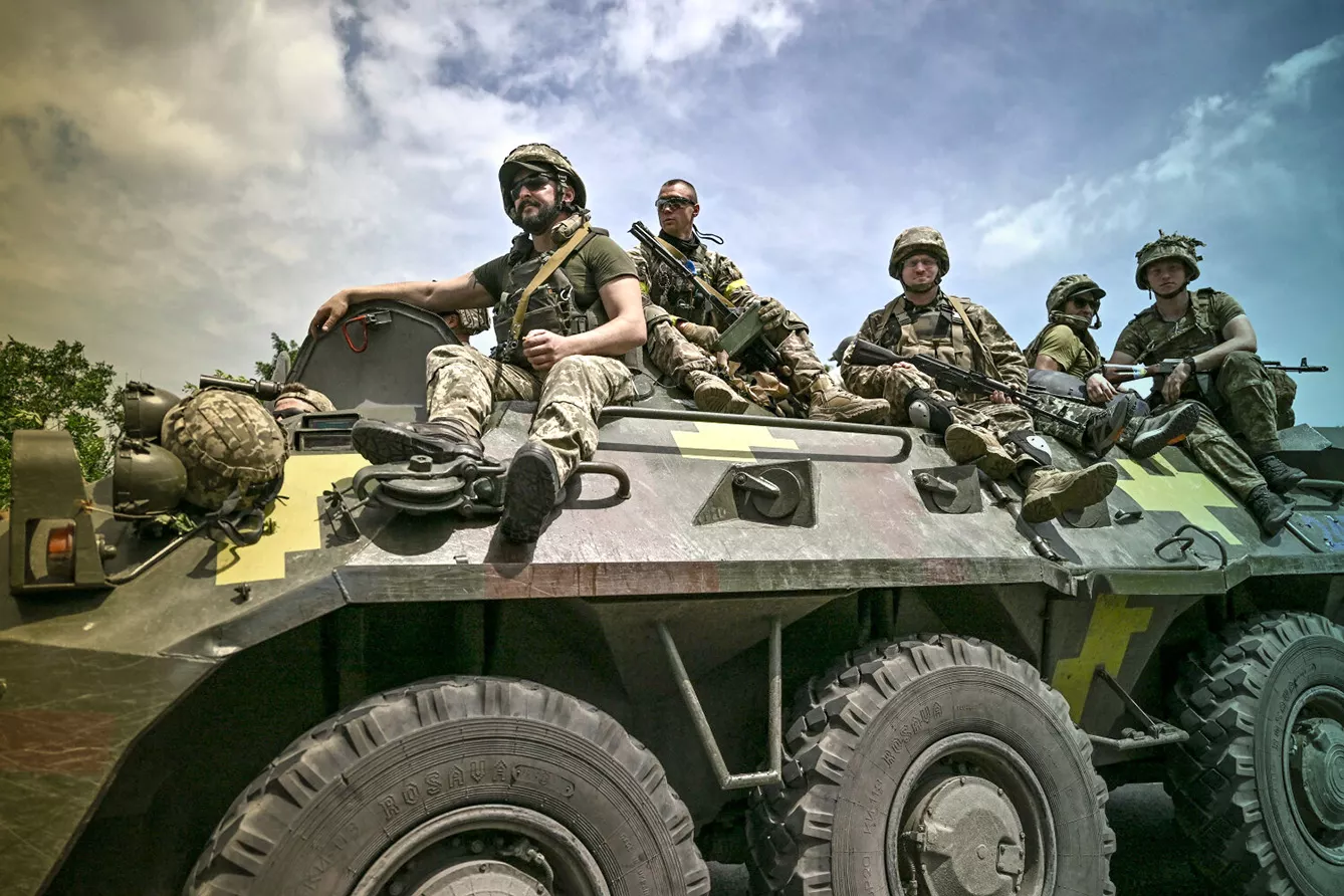Ukrainian troops sit on an armoured vehicle as they move back from the front line