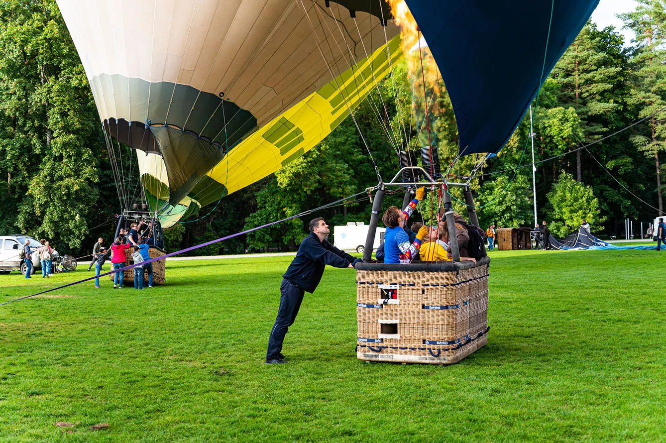 Ground staff man holding the basket with pilot and passengers inside before the launch of hot air balloons at Vingis park in Vilnius