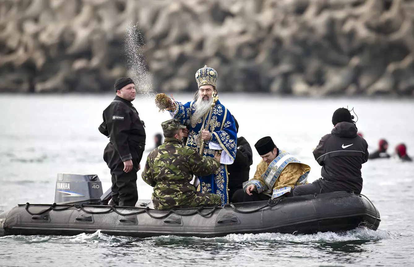 A priest blesses swimmers while riding in a small Romanian navy vessel on the Black Sea