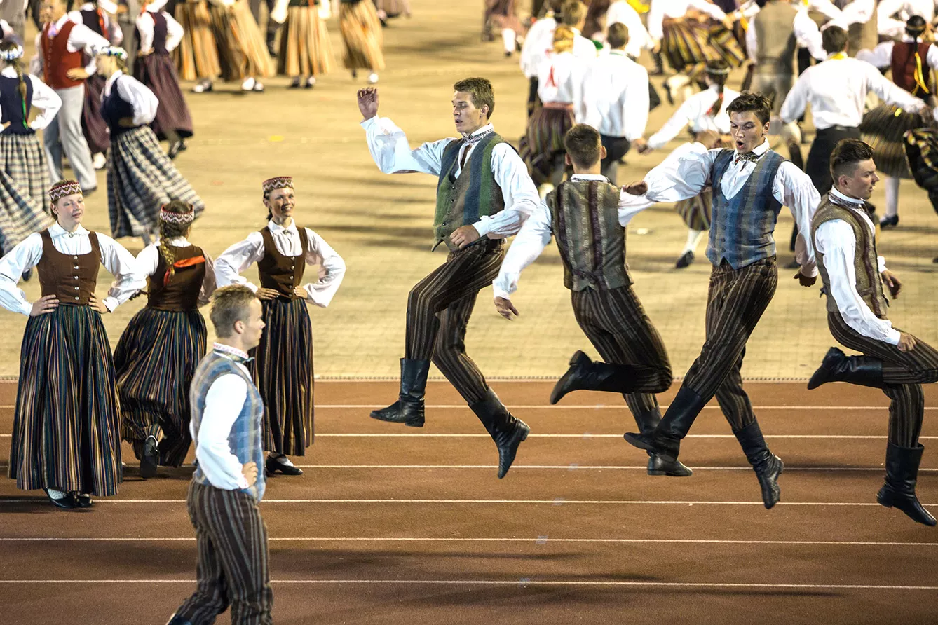 A group of men can be performing the national Latvian dance whilst jumping high up in the air while the women dancers are looking upon them