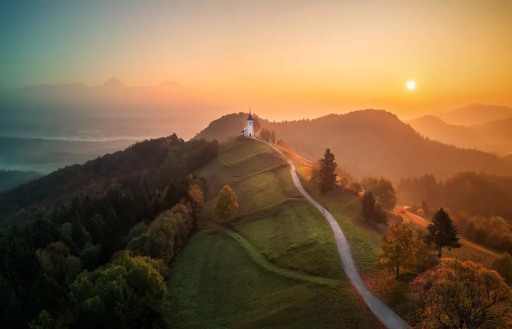 Aerial drone view of small beautiful church on top of a mountain in Slovenia at dawn. Beautiful autumn morning landscape