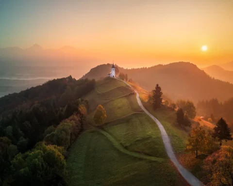 Aerial drone view of small beautiful church on top of a mountain in Slovenia at dawn. Beautiful autumn morning landscape