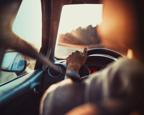 Man driving car, hand on steering wheel, looking at the road ahead,sunset.
