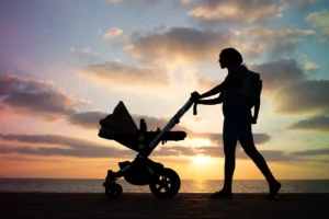 Woman with stroller at sunset, walking on the beach