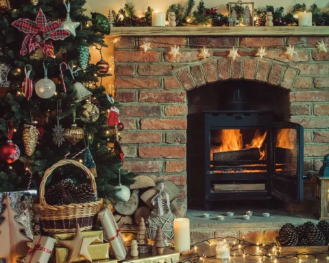 Beautiful Christmas setting, decorated fireplace with woodburner, lit up Christmas tree with baubles and ornaments, lantern, stars and garlands, selective focus