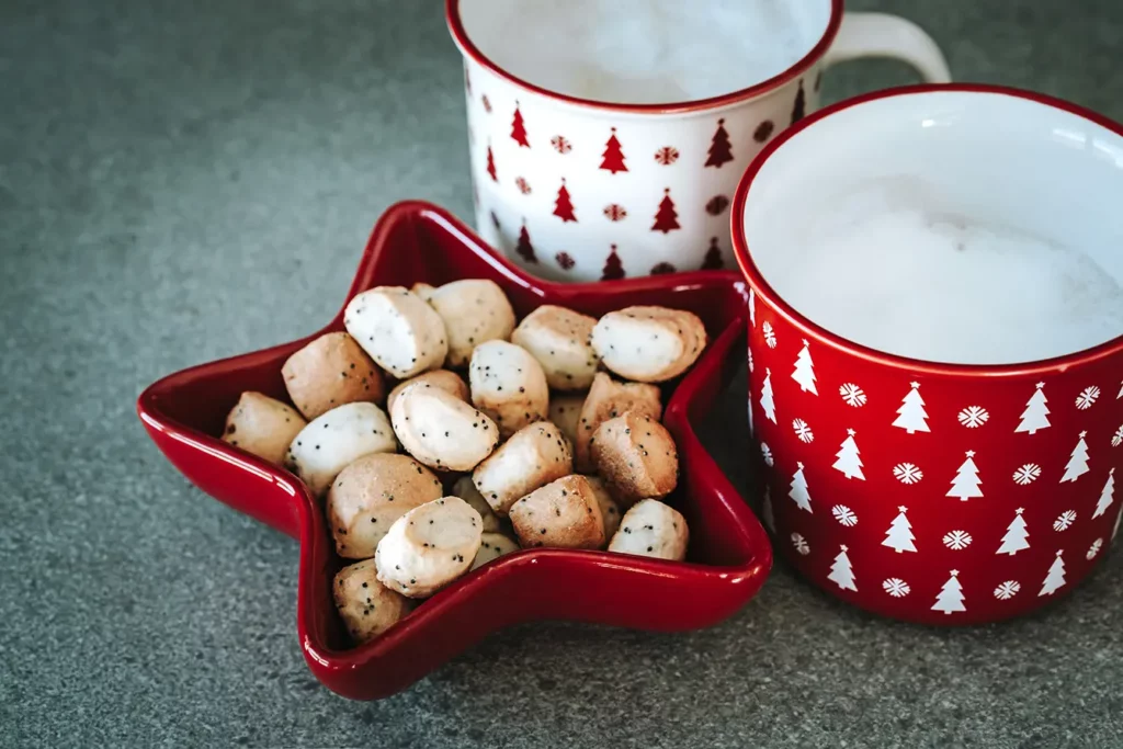 Christmas eve background. Traditional cookies kuciukai in red star shaped vase and two cups of milk. Mugs decorated with Xmas ornaments. Winter holidays concept