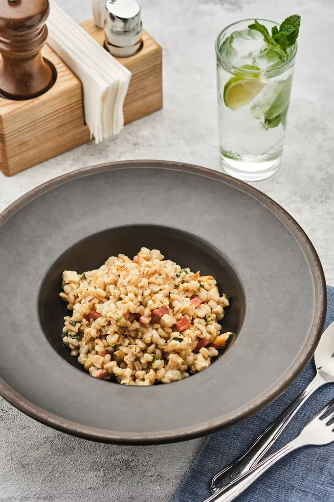 Barley porridge with bacon on a dark plate on a light table