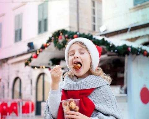 Kid is eating fast food at Christmas market. Cute child is tasting festive sweets, fritters, chocolate doughnuts outside in old town street. Cozy fair atmosphere in Dubrovnik, Croatia