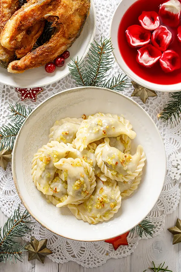 Christmas dumplings pierogi stuffed with forest mushrooms and cabbage on a white plate on a white holiday table, top view. Traditional Christmas eve dish in Poland