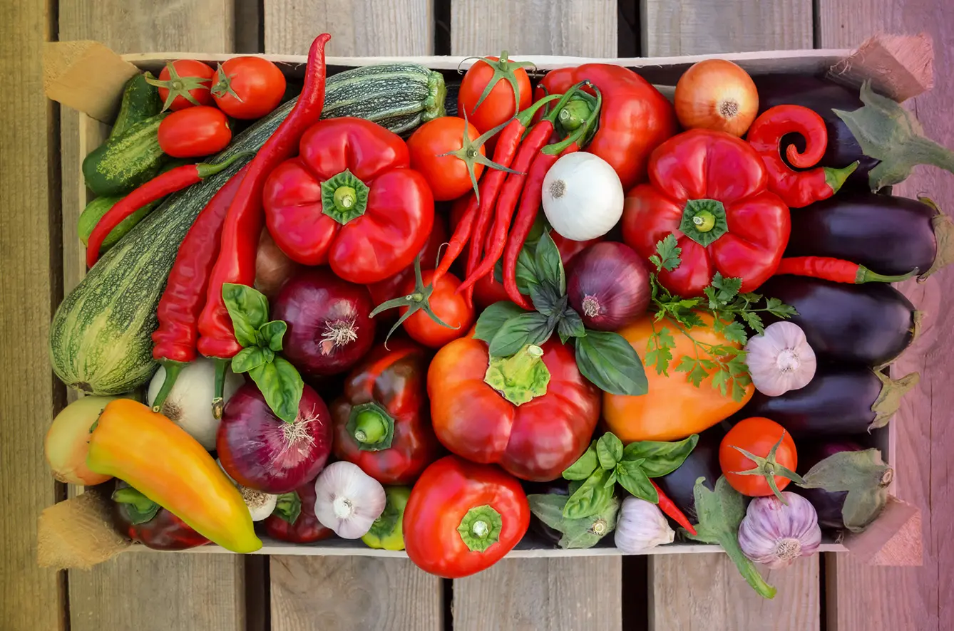 Harvest fresh vegetables in a box on a wooden background, top view
