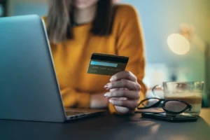 Unrecognizable person's hand holding credit card in front of lap top at home