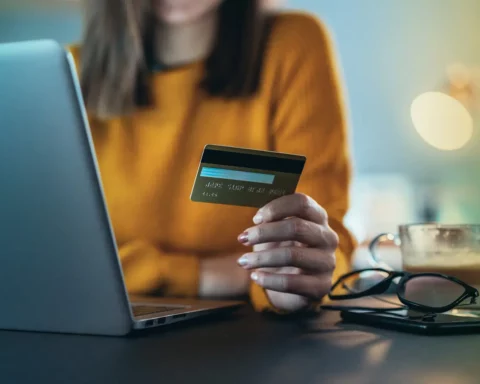 Unrecognizable person's hand holding credit card in front of lap top at home