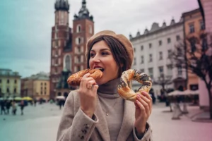 Tourist woman eating bagel obwarzanek traditional polish cuisine snack waling on Market square in Krakow. Traveling Europe in autumn