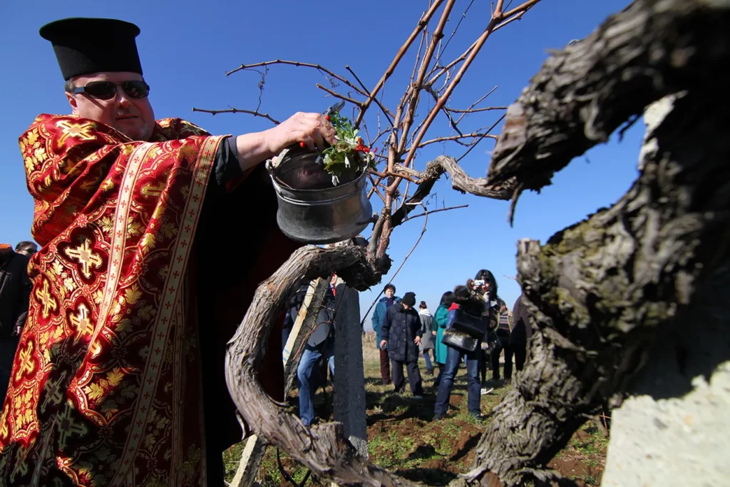 Bulgarian Orthodox priest leads an open air mass as dressed with national traditional clothes people play a dance as part of the celebrating of the wine feast called St. Trifon day