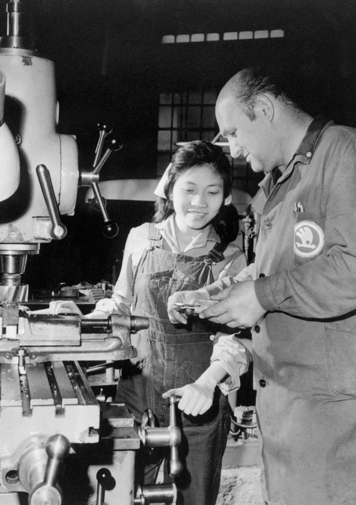 Program for Viet Youth. Plzen, Czechoslovakia: Tran vie Trien of Haiphong is taught to operate a milling machine by foreman Jan Prochazka of the V.I. Lenin works here. She is one of a group of 54 youths from North Vietnam who will take a three-year course in "black" crafts. They will learn to be skilled fitters, metal-pattern makers, turners, tool-makers, and milling machine operators in 1971.