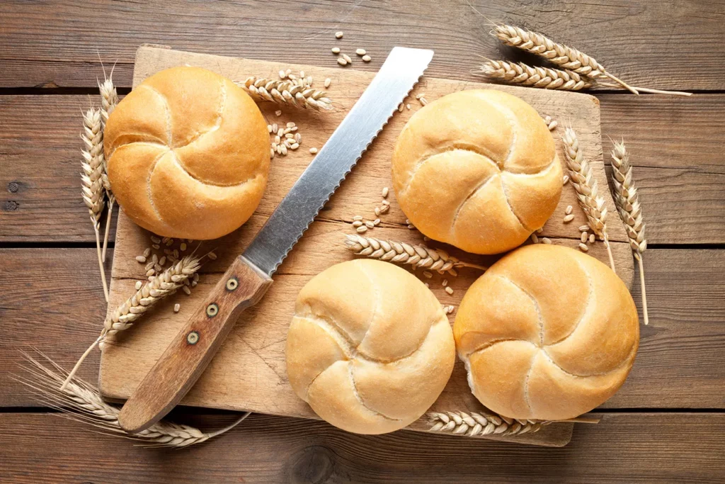 Kaiser rolls with knife and cutting board on old wooden table