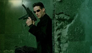 Keanu Reeves as Neo in a scene from the Warner Bros film: The Matrix (1999). Neo takes cover while armed with his Skorpions. Plot: A computer hacker learns from mysterious rebels about the true nature of his reality and his role in the war against its controllers