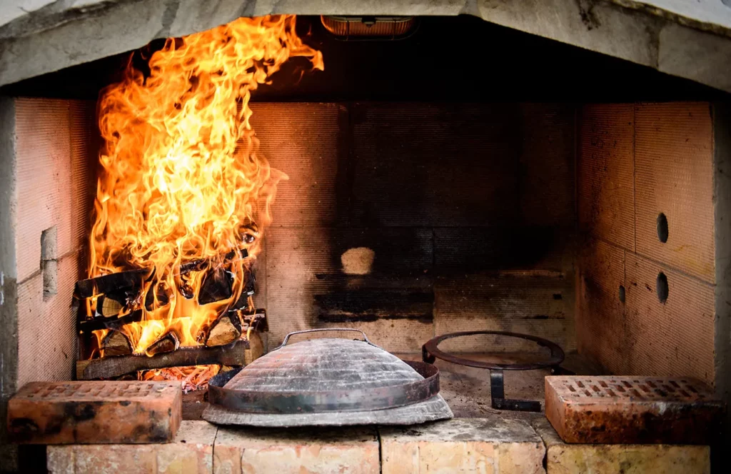 Cooking of traditional Mediterranean Croatian meal Peka in metal pots called sac sach or sache or a metal lid. Fireplace with open fire and burning coals.