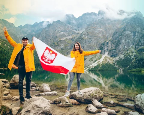 Couple in yellow raincoats holding polish flag in front of lake in Tatra mountains