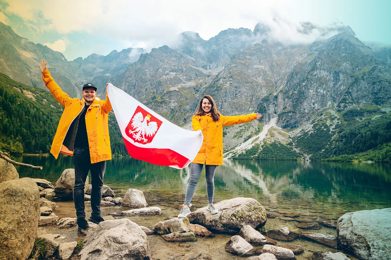 Couple in yellow raincoats holding polish flag in front of lake in Tatra mountains