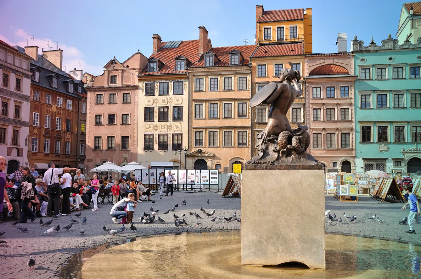 Warsaw, Poland. Main Square of the Old Town. Warsaw Mermaid - symbol of the city - in front on the right side, many tourists looking visiting the place and feeding pigeons on the left side, and the colorful antique tenements in the background.