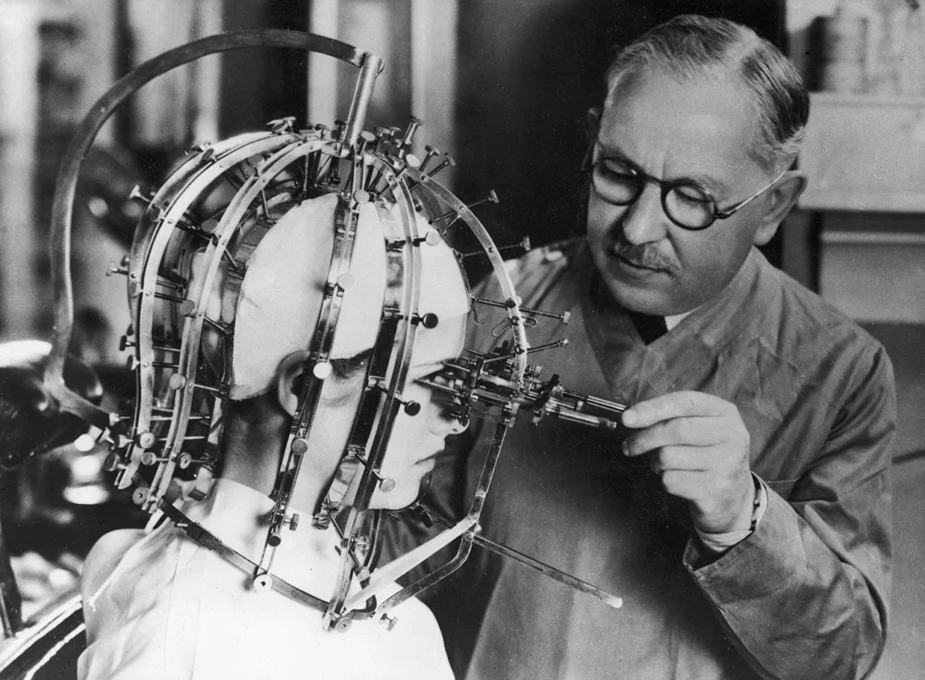 Movie makeup specialist Max Factor, while working on actress Dorothy Wilson, wearing a device to measure facial proportions.