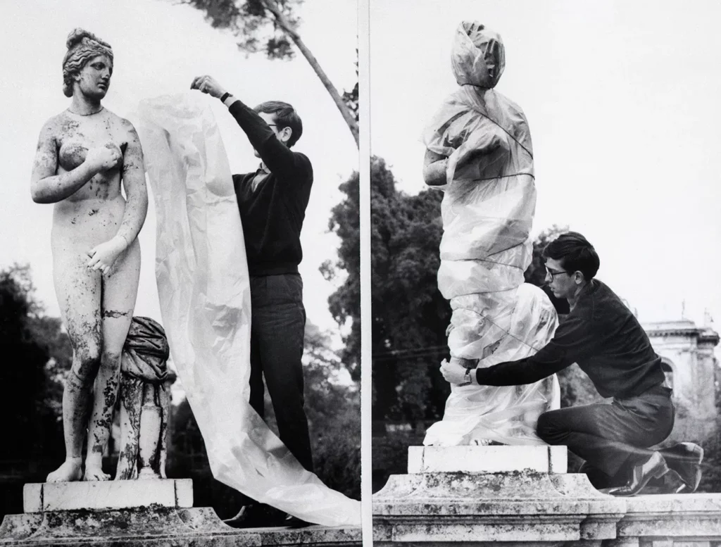Christo Wrapping Ancient Sculpture. 11/29/1963-Rome, Italy- Demostrating his wrap-it art, Christo applies a polythene sheet to an ancient sculpture in Rome. With the plastic sheet and some string, Christo explains, "The sculpture takes on the loving form of mystery."