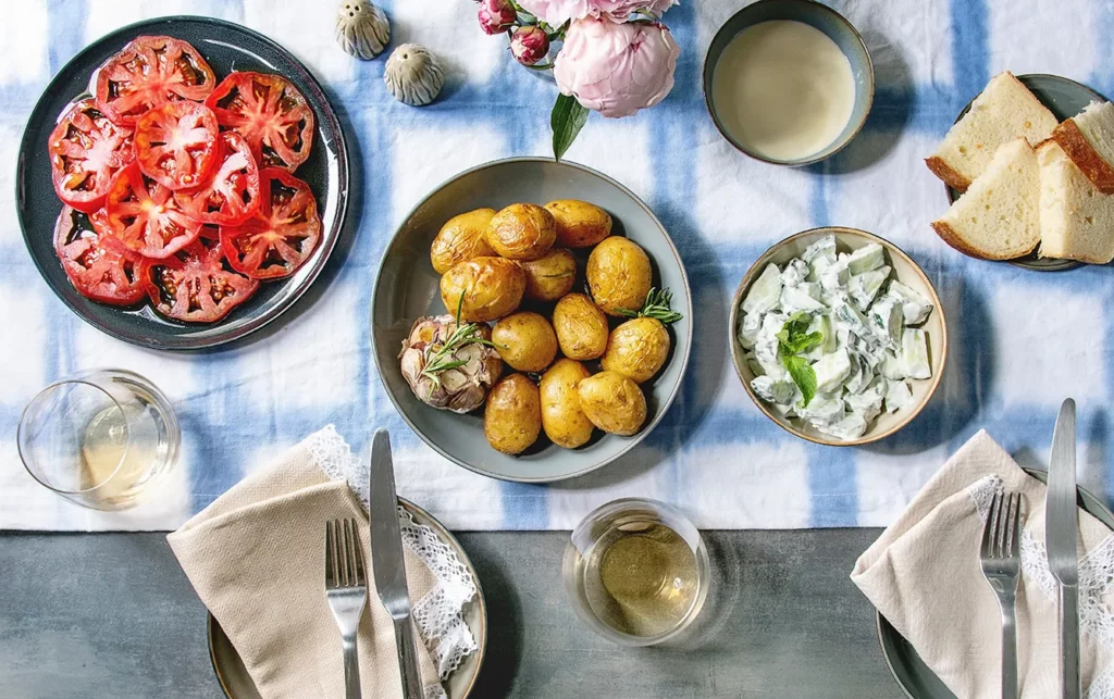 Young baked potatoes, tomato carpaccio, cucumber salad, bread, wine, sauce and flowers