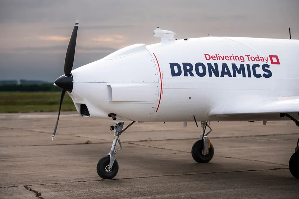 The left side of the pzodu drone on the runway, featuring dronamics company logos with the slogan Delivering today.