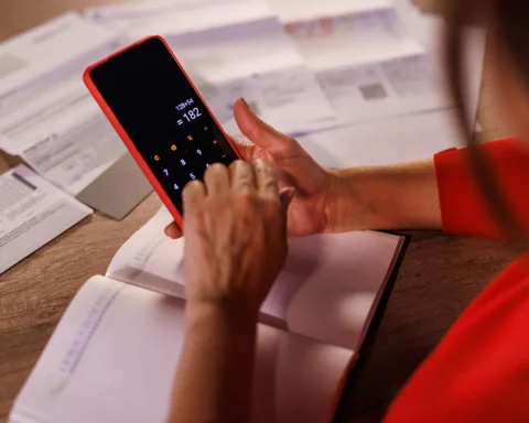 Close up shot of woman sorting out expenses, bills and finances at home and using a calculator on her smartphone.