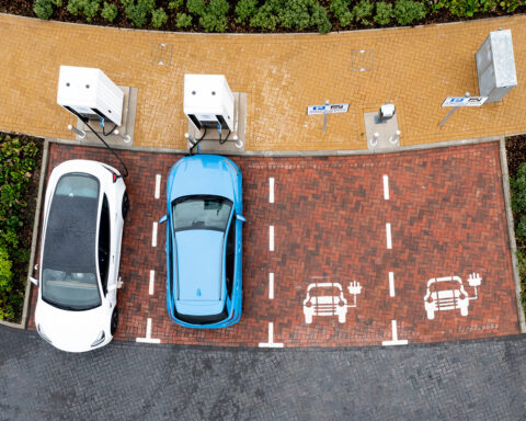 An aerial view directly above electric cars being charged at a motorway service station car charging station.