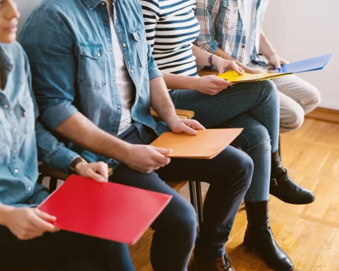 People sitting on chairs with folders before job interview in waiting room.