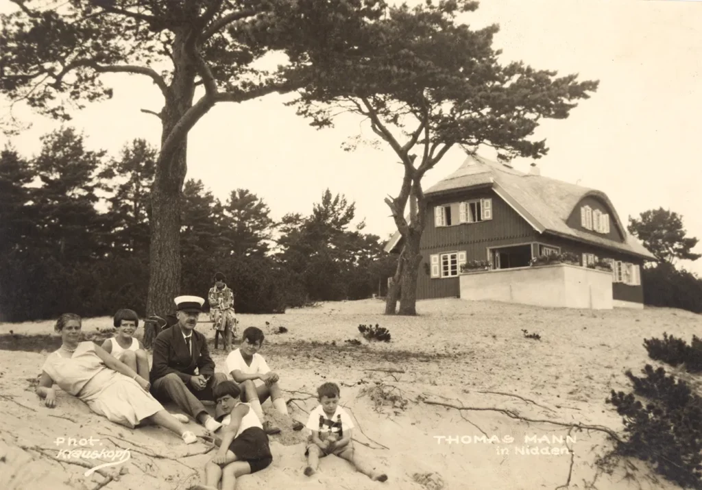 Stay in Nidden. At the holiday home. Sitting in the sand from left: Katia Mann, Elisabeth Mann, Thomas Mann, Michael Mann, unknown boy, Alexander Ferber (son of the girl Maria Ferber), on the bench in the background Monika Mann. 1930.