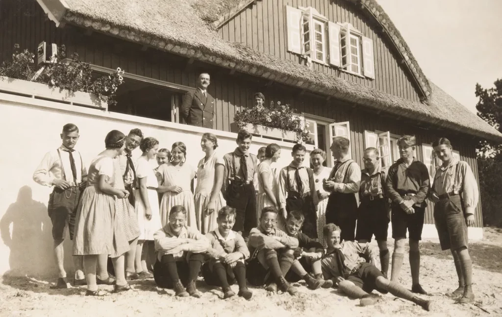 Stay in Nidden. Thomas Mann and unknown person standing on the terrace of the holiday home, a group of young people in front of it, 1930.