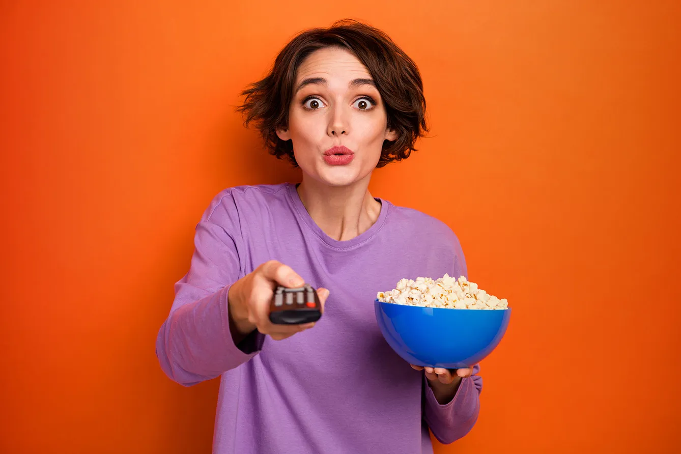 Portrait of impressed nice girl hold popcorn plate switch tv program isolated on orange color background.