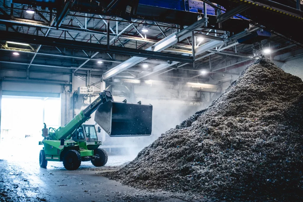 Indoor view of heavy machinery scooping up shredded recyclables from pile on facility floor to be further processed. Recycling center in Ljubljana.