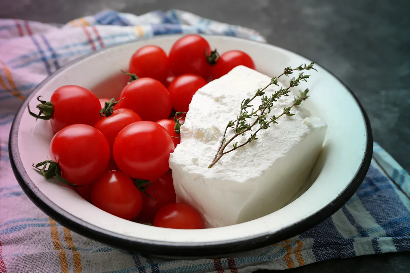 Bowl with tasty bulgarian cheese and tomatoes on grey background