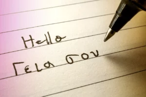 Beginner Greek language learner writing Hello word in greek alphabet on a notebook